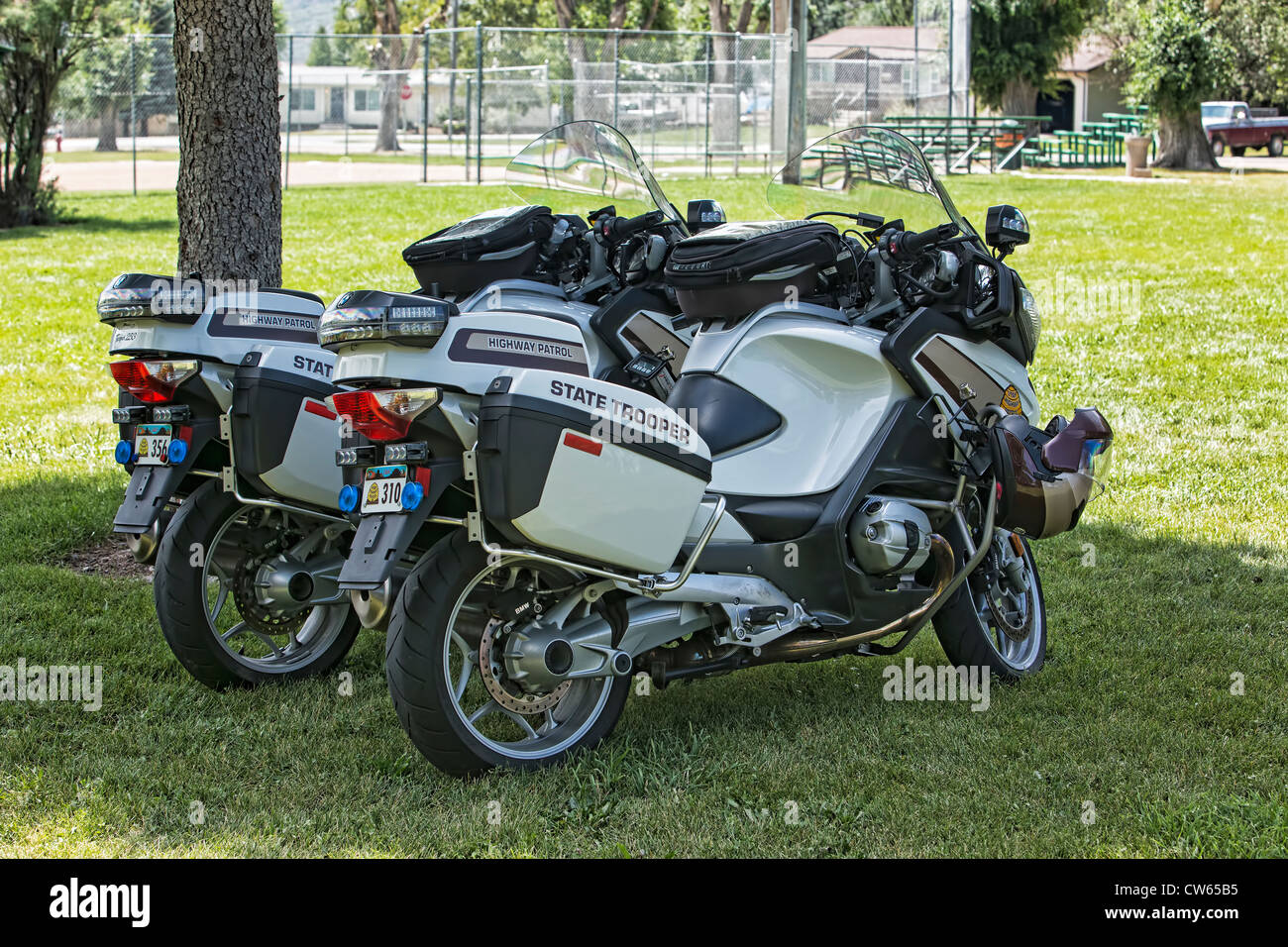 Two State Trooper motorcycles parked under a tree in a city park, used as escorts for a car show. Stock Photo