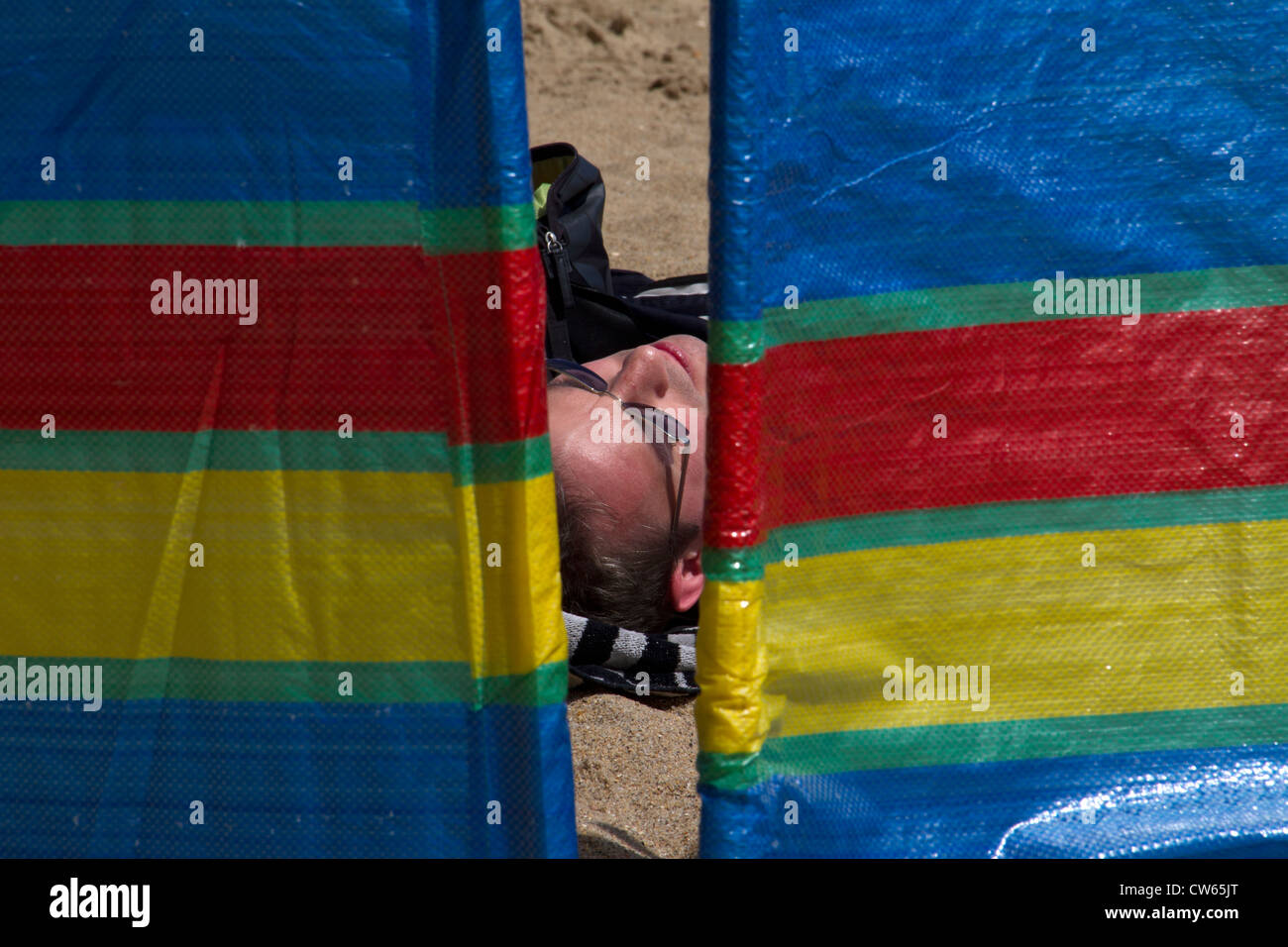 A man sleeps on Swanage beach, as seen through a windbreak. Stock Photo