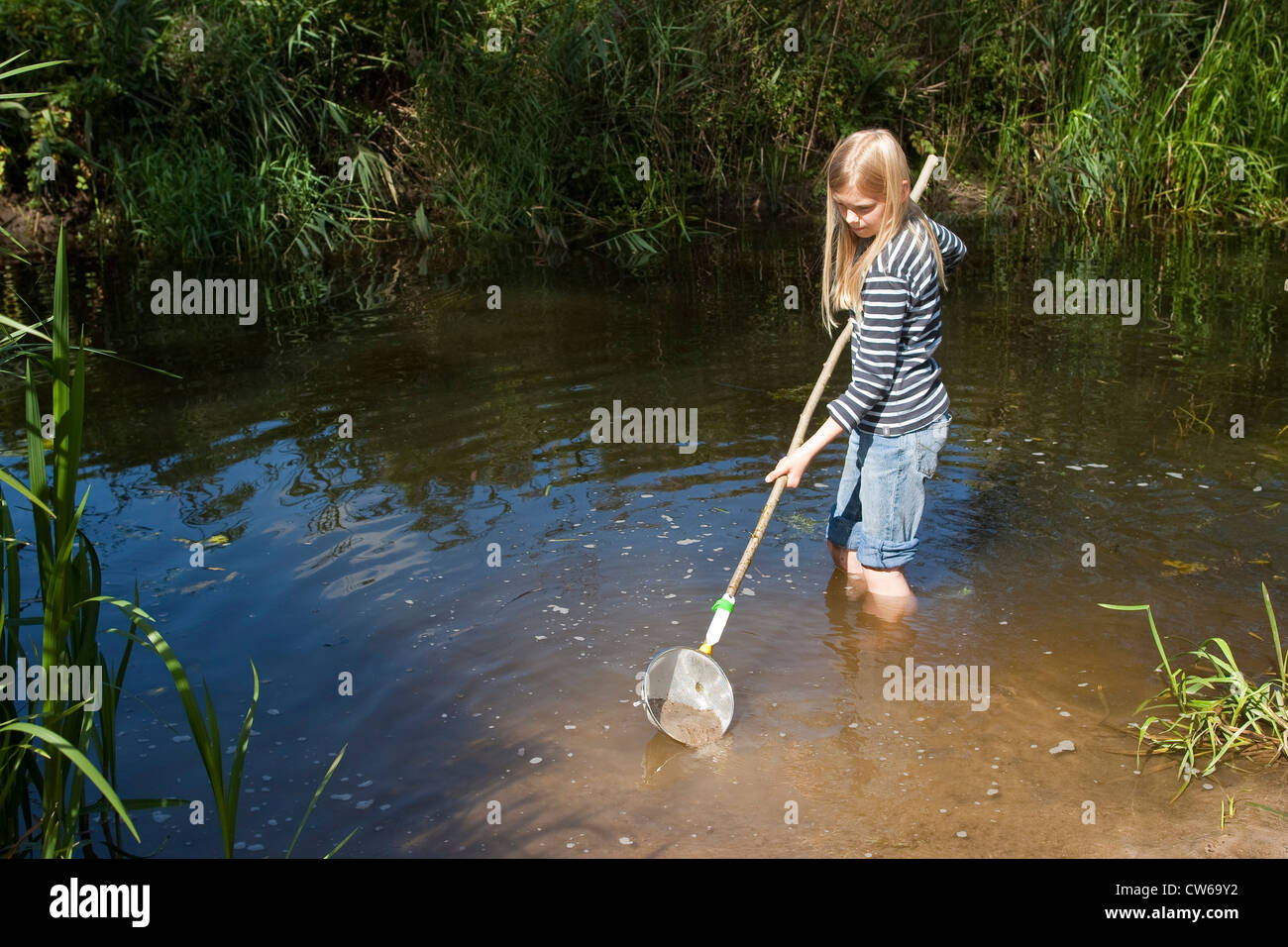 girl with a selfmade dip net, made from a colander, standing in a creek Stock Photo