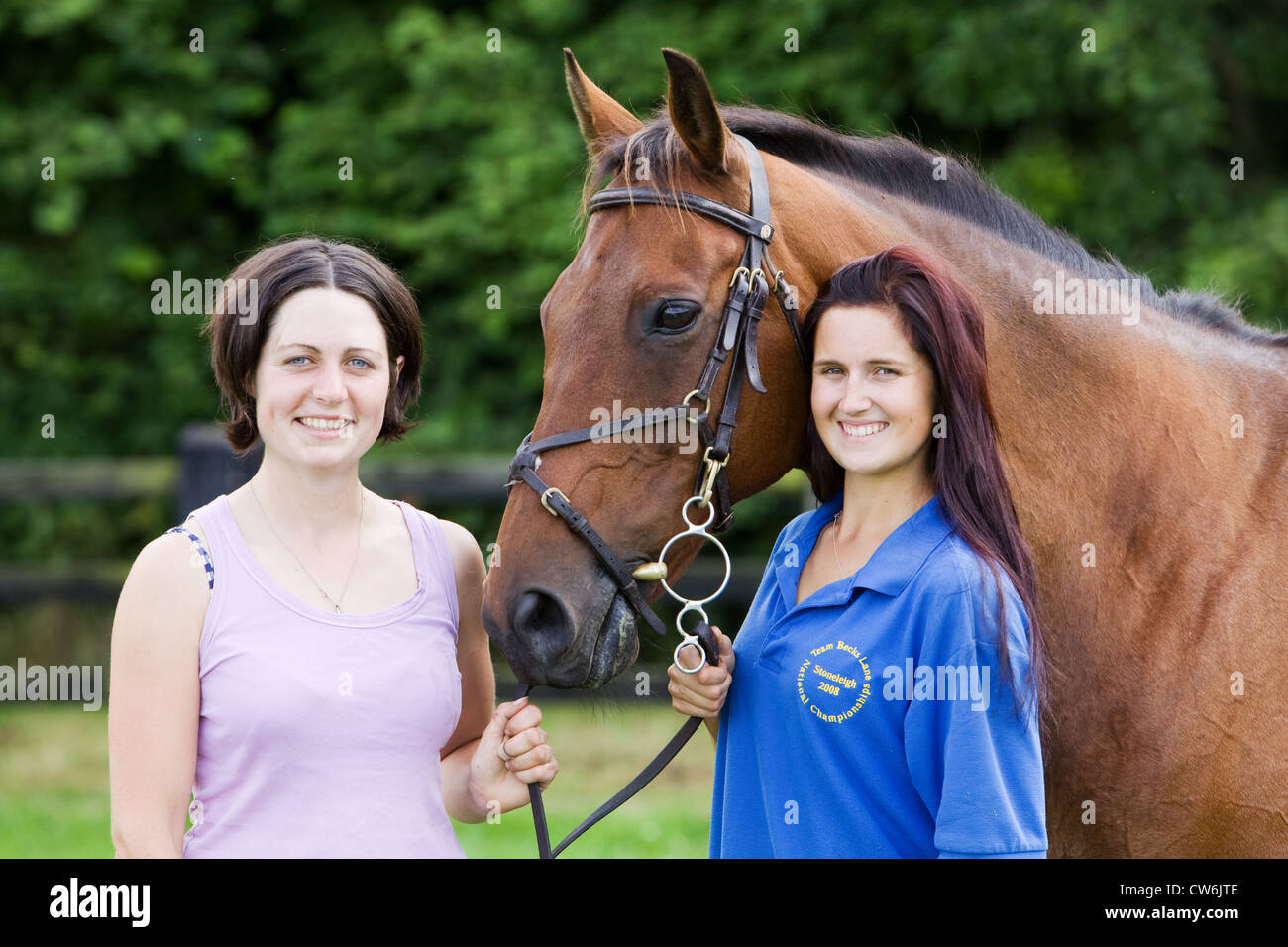 Two young women standing with a horse in a grass paddock in the English countryside in summer Stock Photo