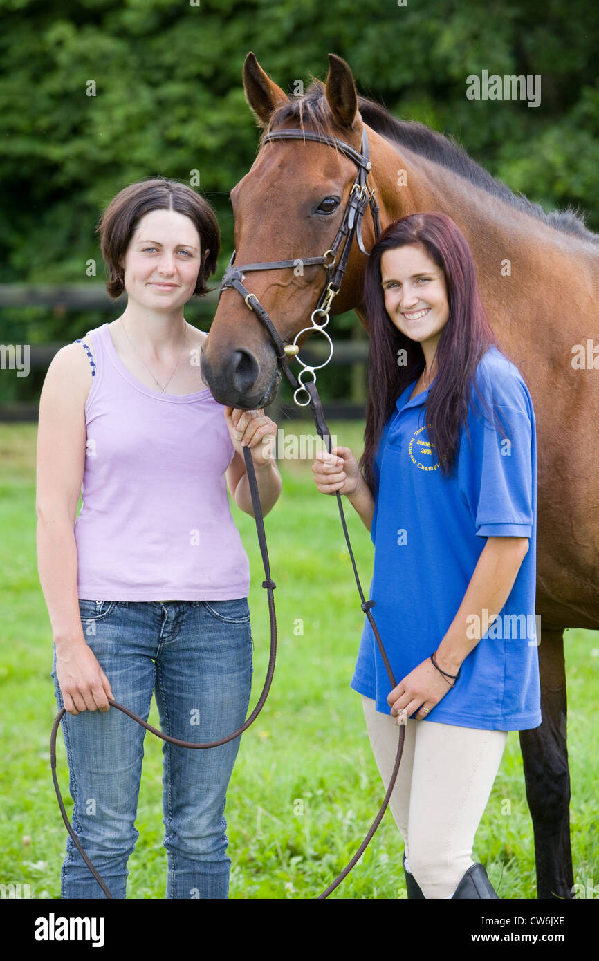 Two young women standing with a horse in a grass paddock in the English countryside in summer Stock Photo