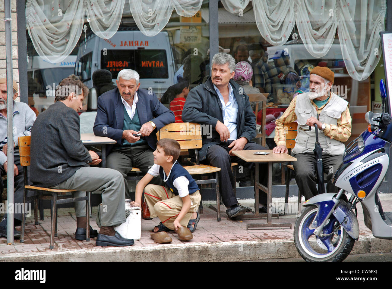 shoeshine boy cleaning shoes of men sitting in front of a cafe, Turkey, East Anatolia, Yusufeli Stock Photo