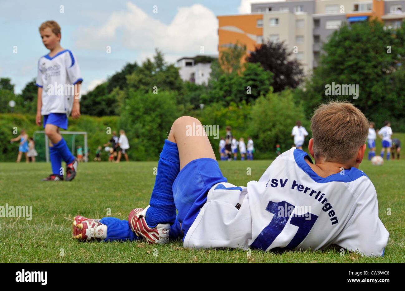 break at a juvenile football tournament, in the foreground a boy lying and relaxing on the lawn
