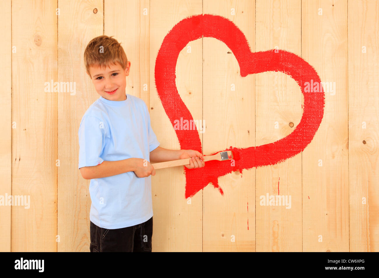 boy painting a heart onto a wooden wall with red paint Stock Photo
