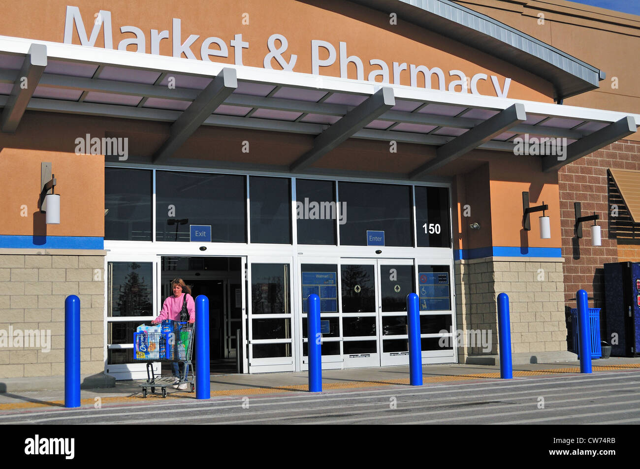 Elmhurst, Illinois, USA. A lone woman shopper exits a mall grocery / drug store with a cart full of products including beer. Stock Photo