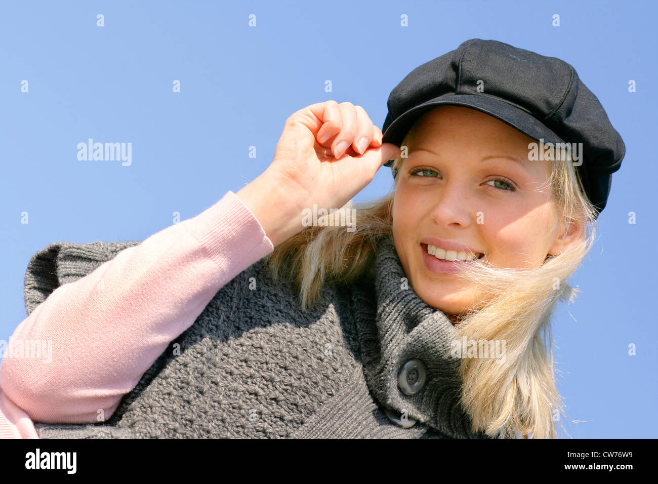 young blond smiling girl, with one hand at her cap Stock Photo