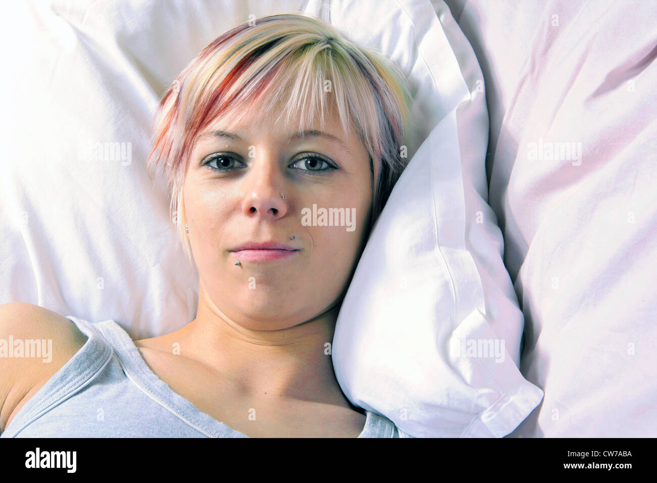 young woman with trendy coloured hair lying in bed, Germany Stock Photo