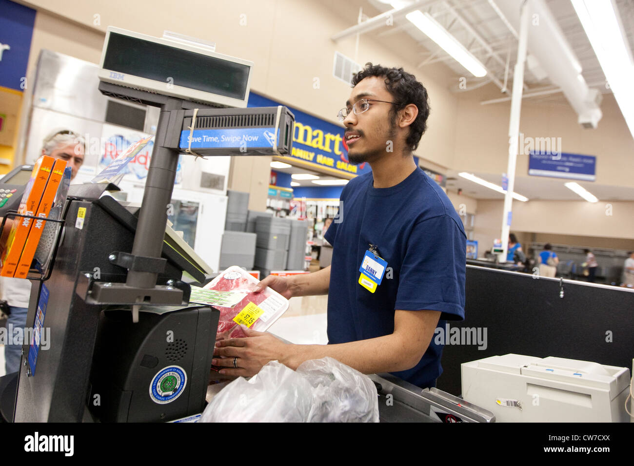 Smiling young Hispanic male cashier rings up products for customer at a Wal-Mart Supercenter in San Marcos, Texas Stock Photo