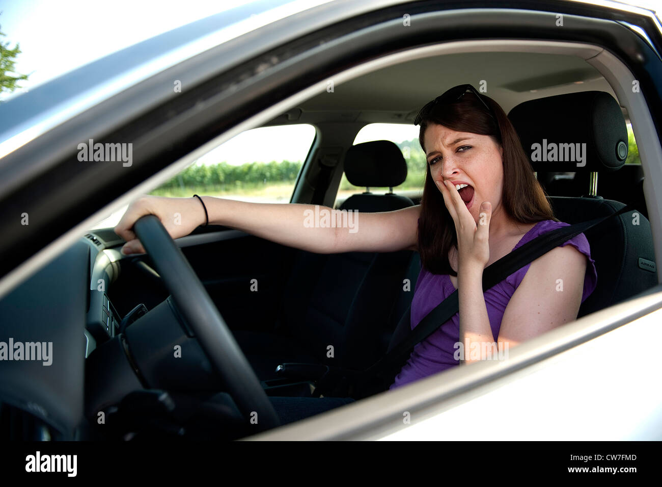 young woman sitting at the wheel of a car yawning Stock Photo