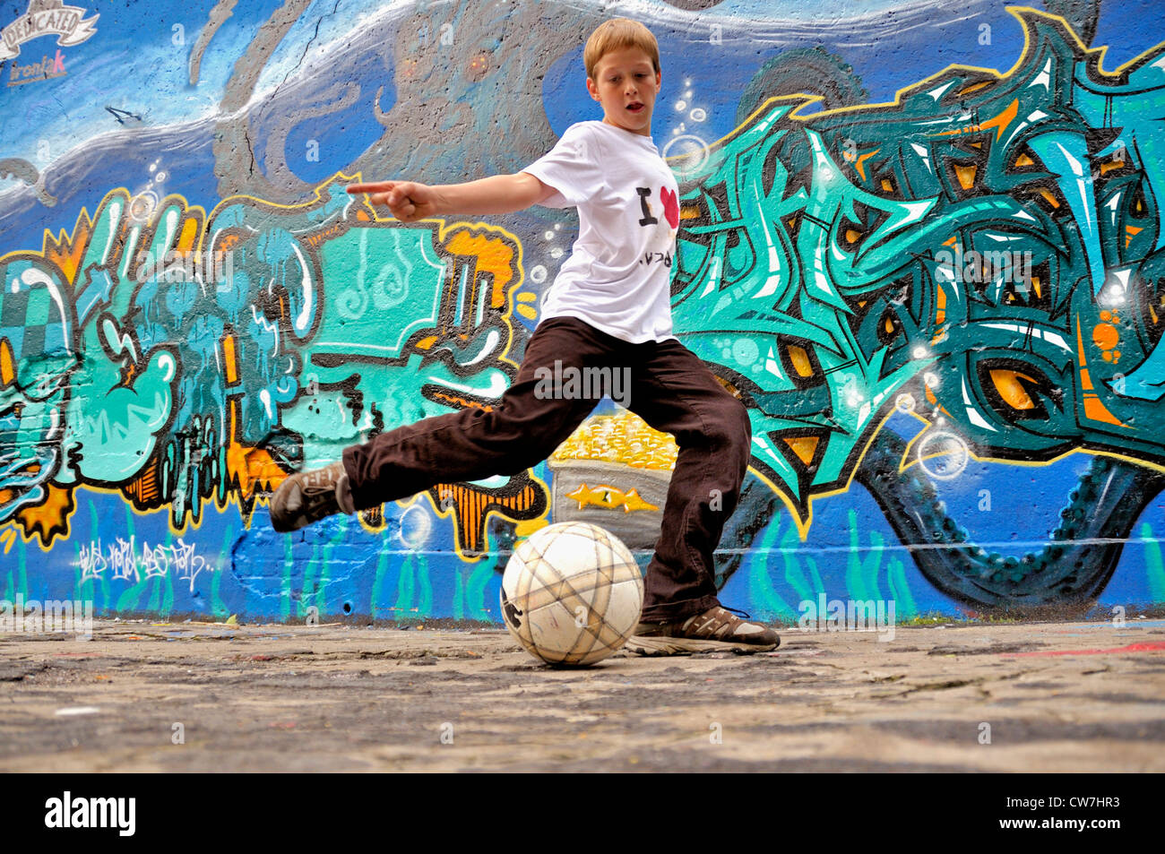 ten years old boy playing football in the street, Germany Stock Photo