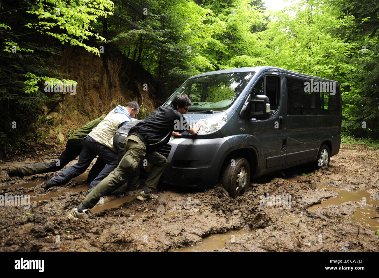 four men pushing a minibus out of mud, Italy, Calabria Stock Photo