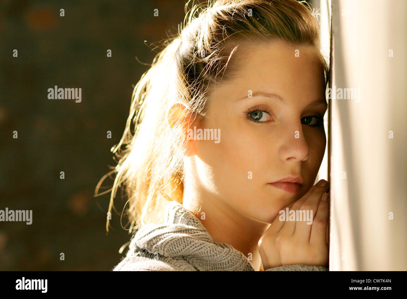 young blond woman leaning against a wall Stock Photo