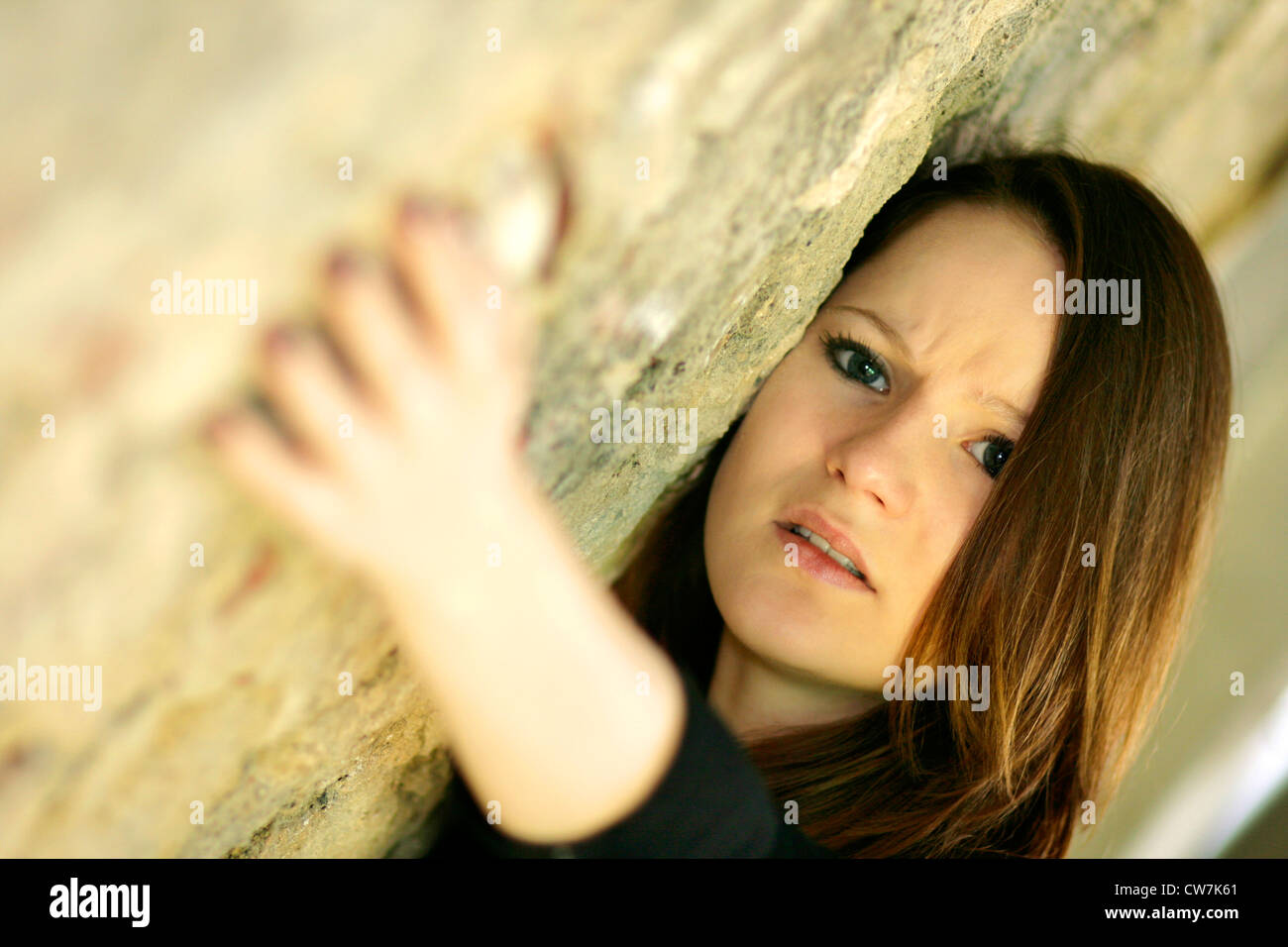 young woman with long brown hair leaning against a wall Stock Photo