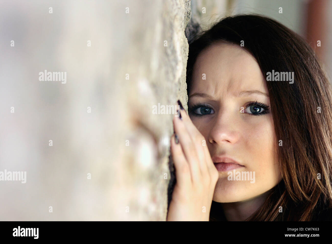 young woman with long brown hair leaning against a wall Stock Photo