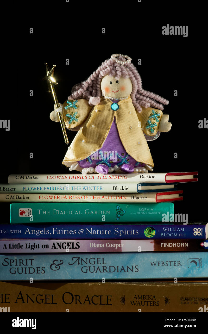Childs Angel doll sitting on spiritual angel books lit by sunlight against a dark background Stock Photo