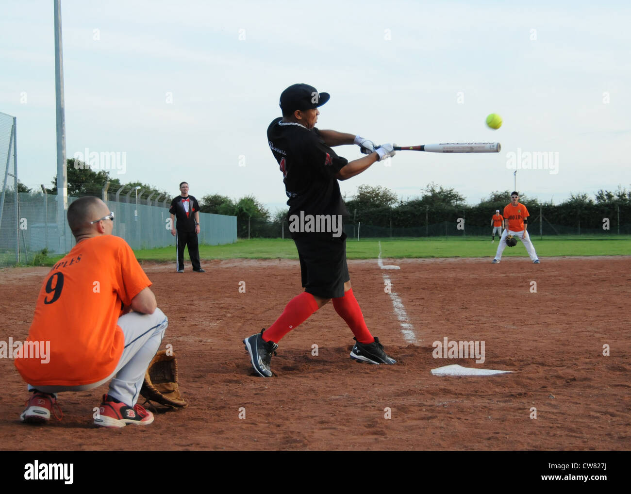 Brandon Burress, 100th Security Forces Squadron, hits the ball as Gabriel Temples, 100th Logistics Readiness Squadron, catches during the Team Mildenhall intramural softball championship, Aug. 14, 2012. The 100th LRS defeated the 100th SFS 8 â€“ 4 to claim the championship trophy. Stock Photo