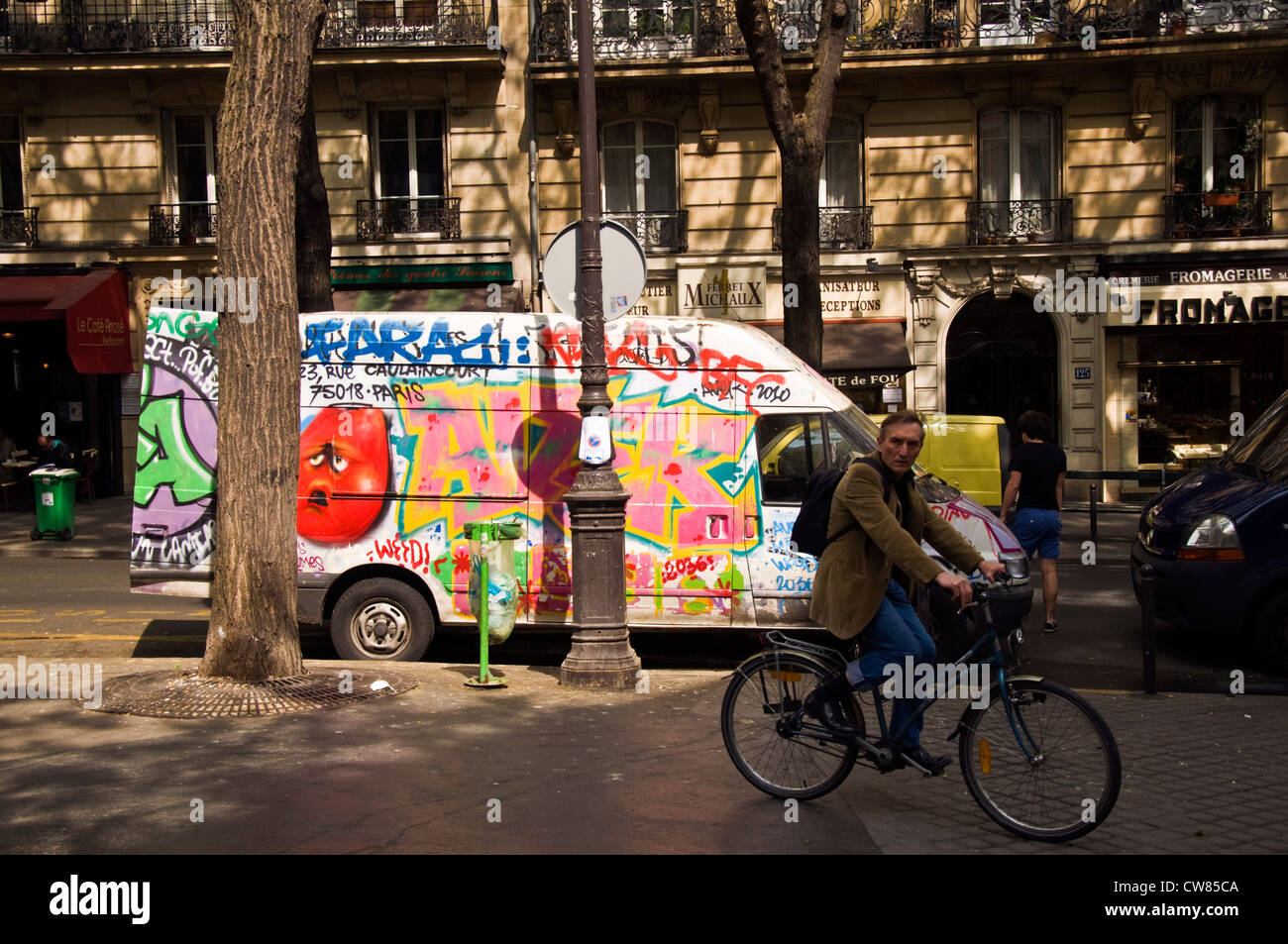 Parisian man cycles on the pavement past a grafftied van in Montmartre district Stock Photo
