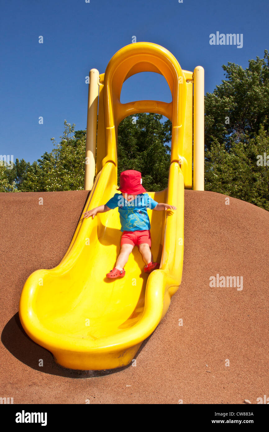 Little girl in red and blue slide on a plastic yellow one in a summer sunny day Stock Photo