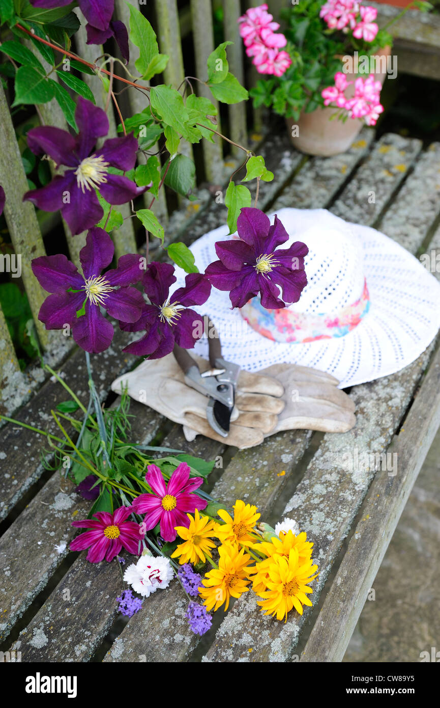 Garden seat with cut summer flowers with ladies sun hat, gloves and secateurs Stock Photo