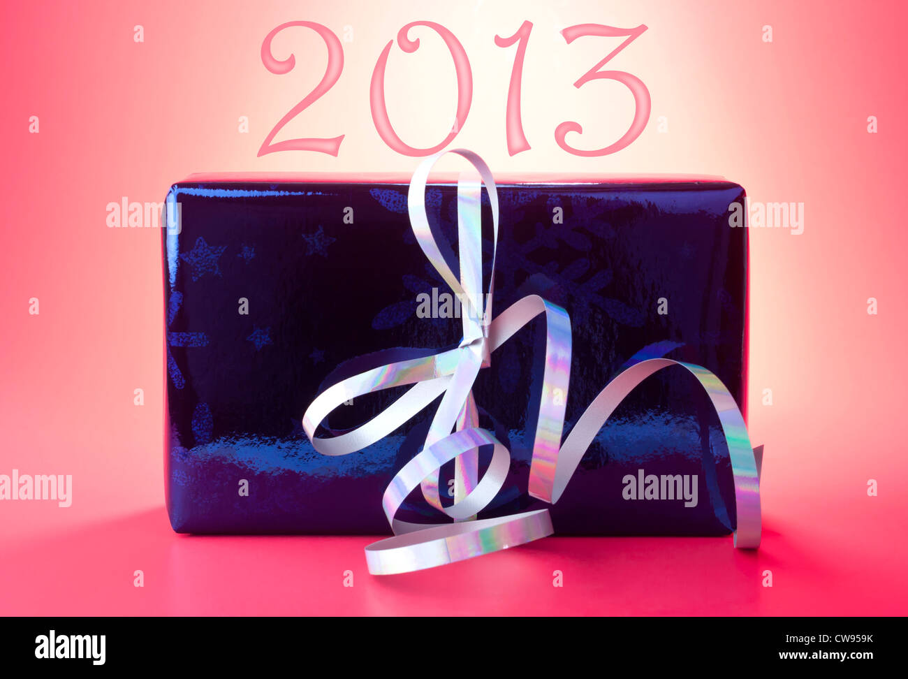 2013 New Year present or gift wrapped in blue shiny wrapping paper with silver curly ribbon against red background. Stock Photo