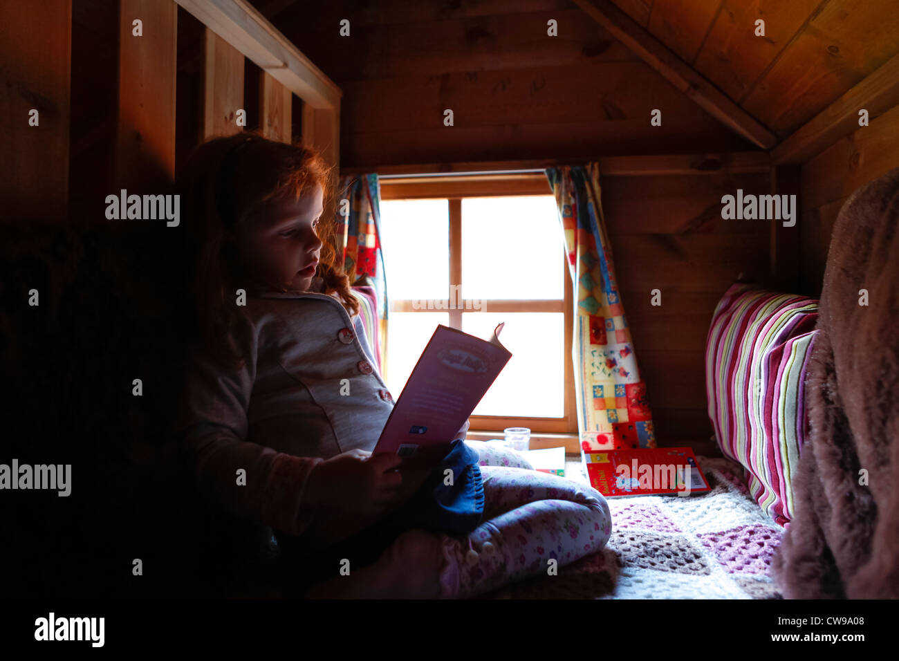 Little girl reading a book in her playhouse den Stock Photo