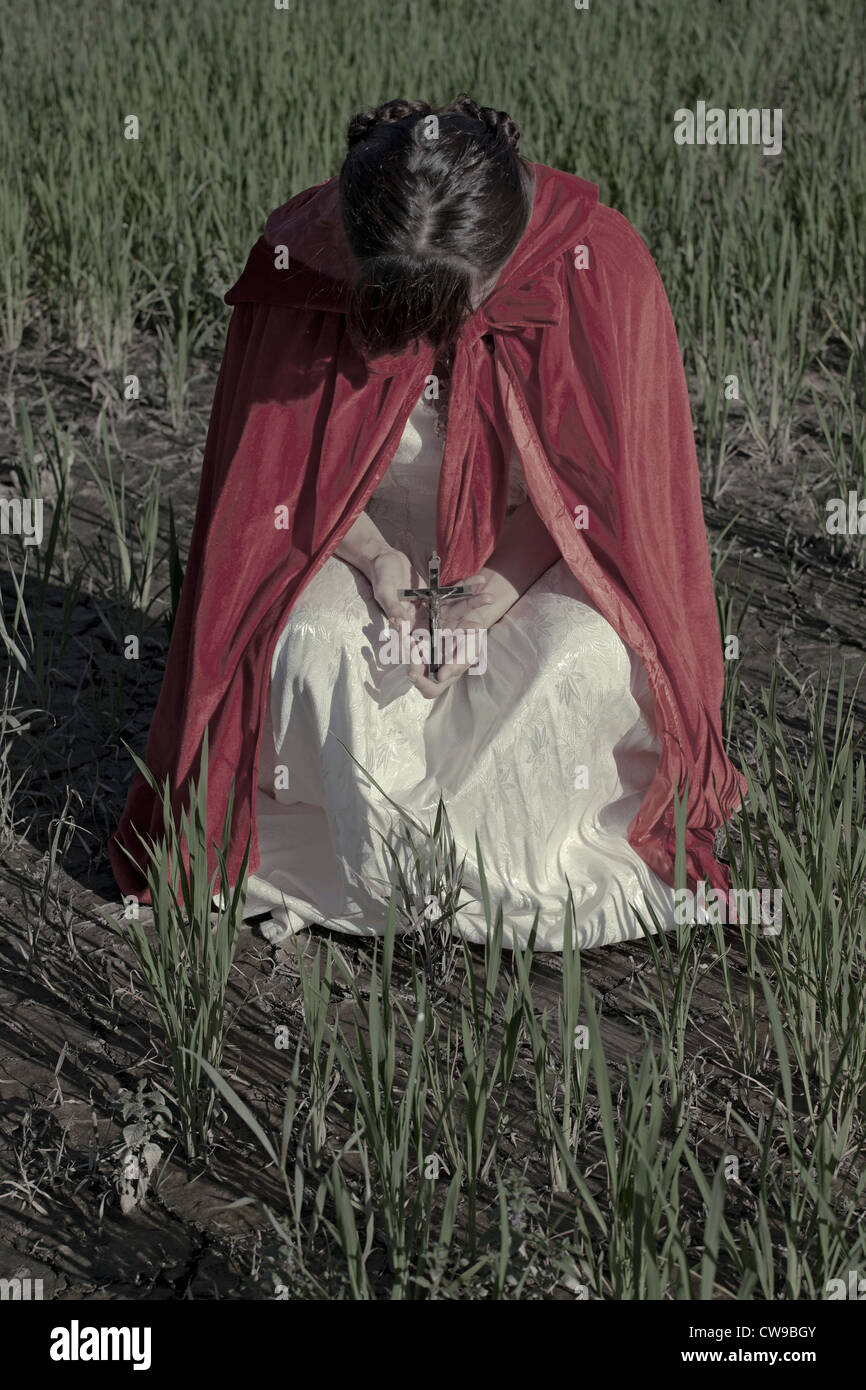 a woman in a red cloak holding a crucifix in her hands Stock Photo