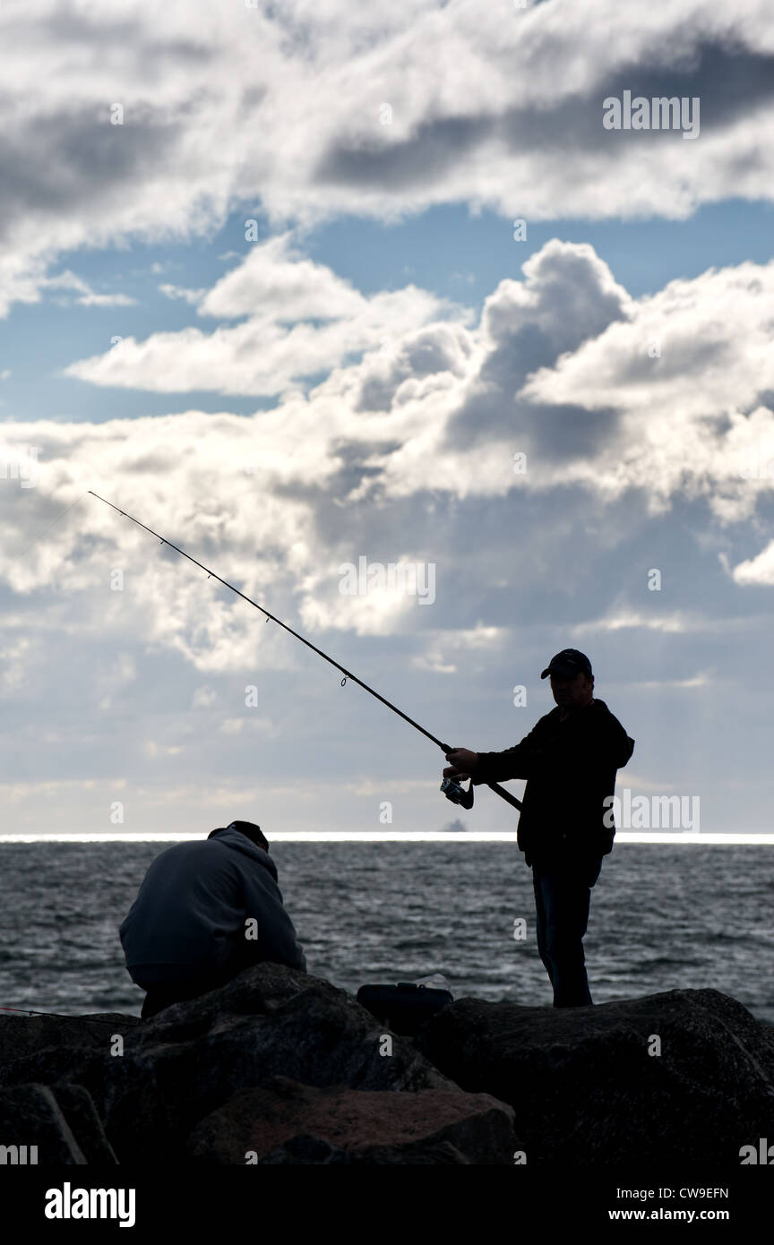 An angler fishing off rocks at Cottesloe Beach in Perth, Western