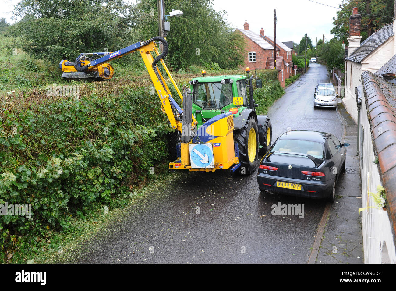 Car overtaking tractor hedge cutting Uk Stock Photo