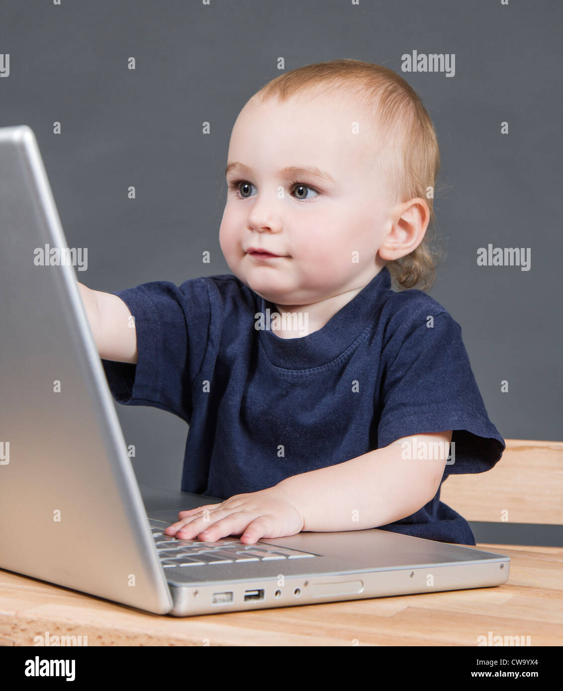 young child with laptop computer on wooden desk in grey background Stock Photo