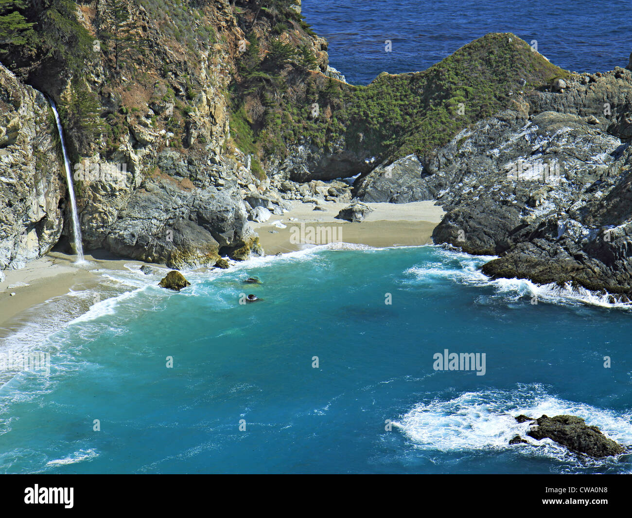 Beautiful waterfall pouring onto beach in blue ocean cove. Stock Photo