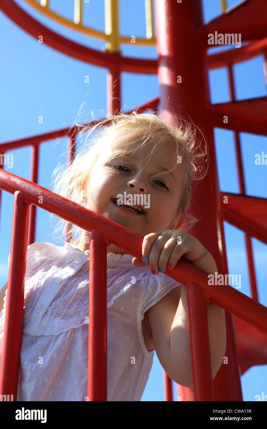 Three year old blond girl climbing the stairs of a chute at the play park Stock Photo