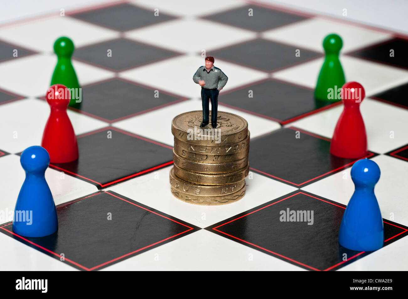 Stacked up one pound coins and toy figure on top of it, surrounded by pawns on a checked board Stock Photo