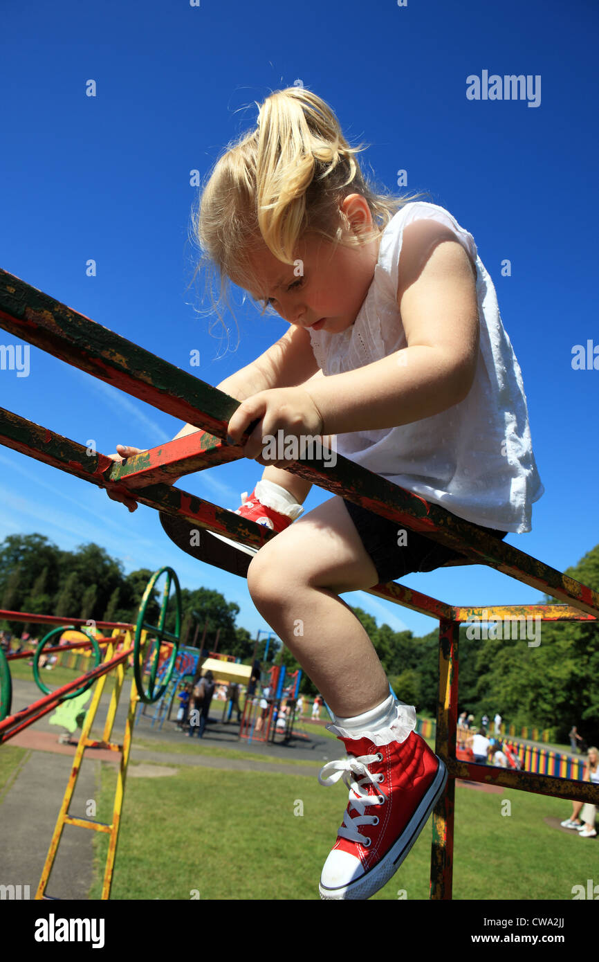 Three year old blond girl playing on a climbing frame at the swing park on a sunny summers day Stock Photo