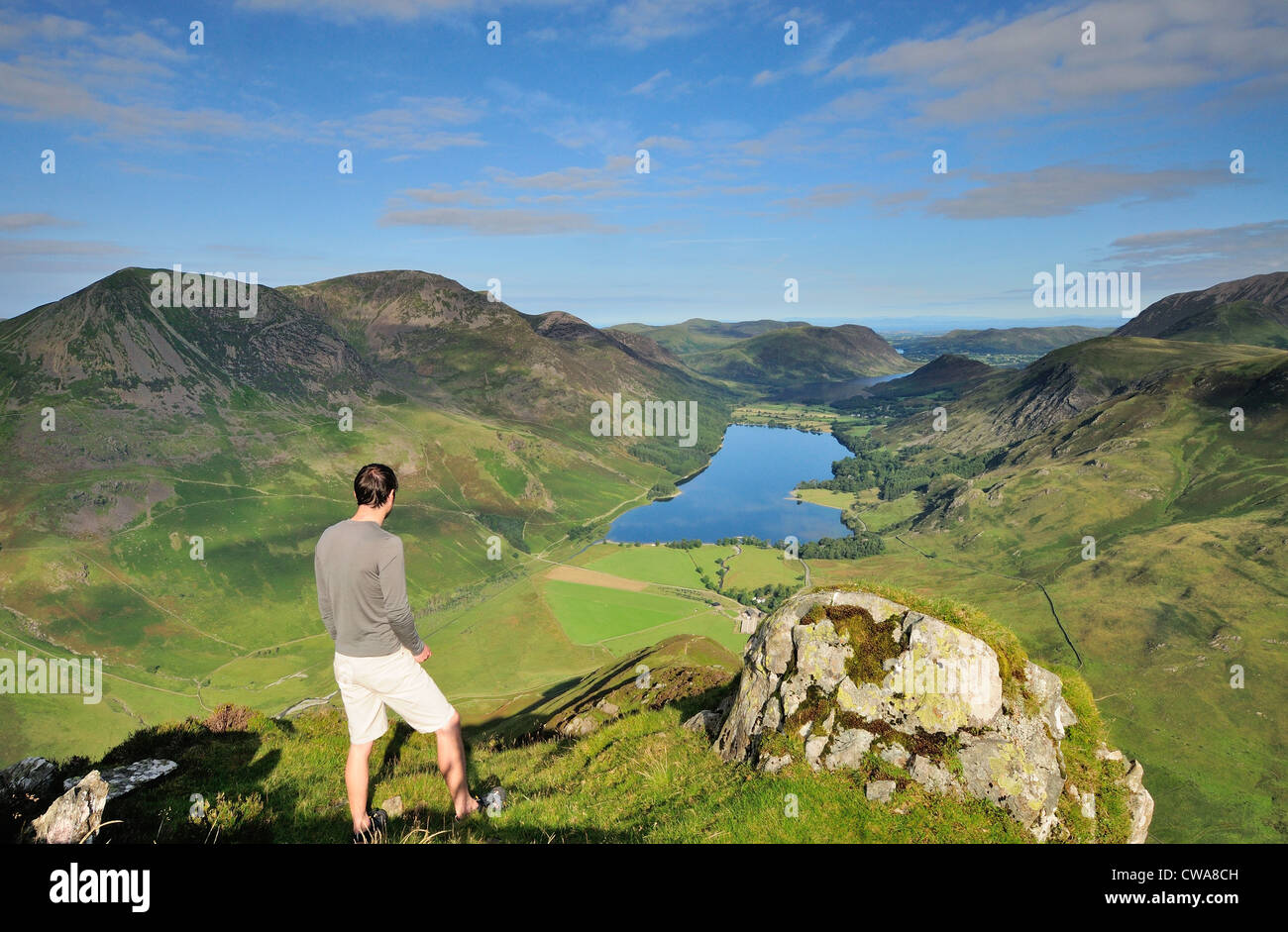 Walker admiring the view over Buttermere from Fleetwith Pike on a sunny summer blue sky day in the English Lake District Stock Photo