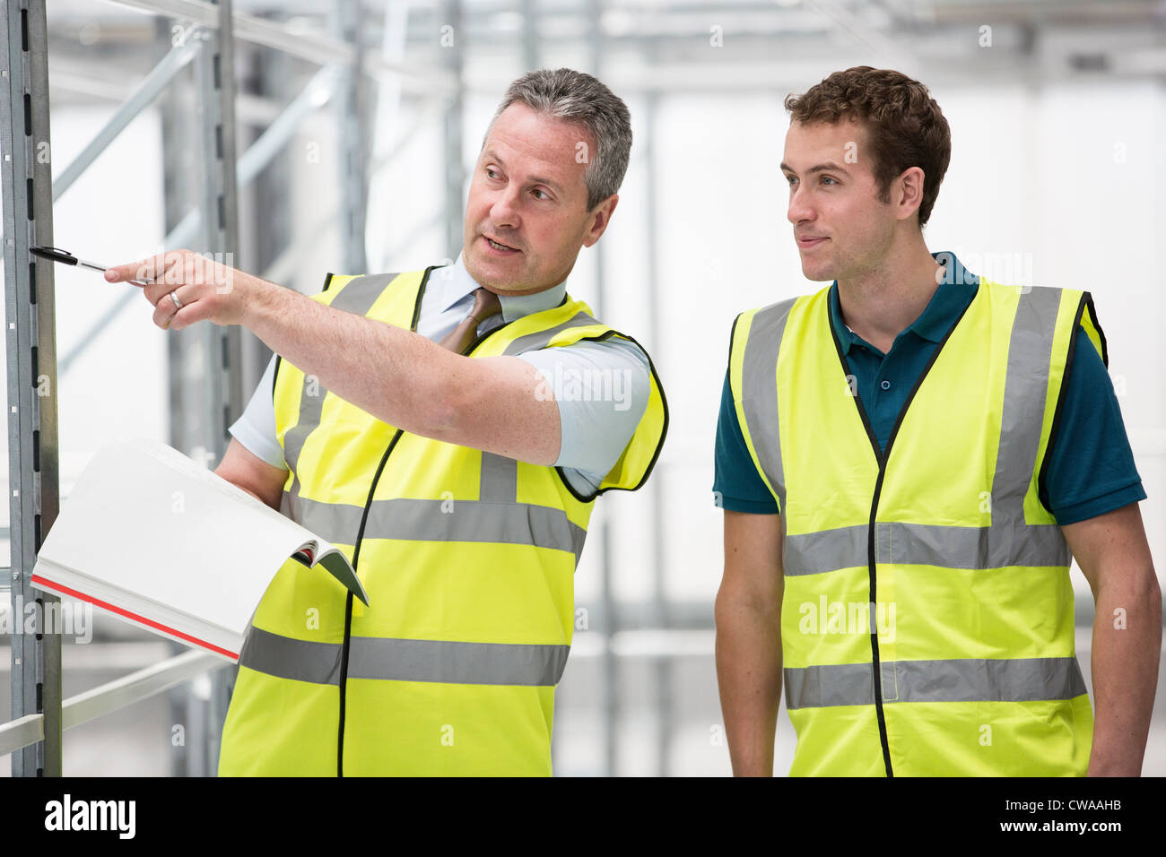 Two men in warehouse, one pointing with pen Stock Photo