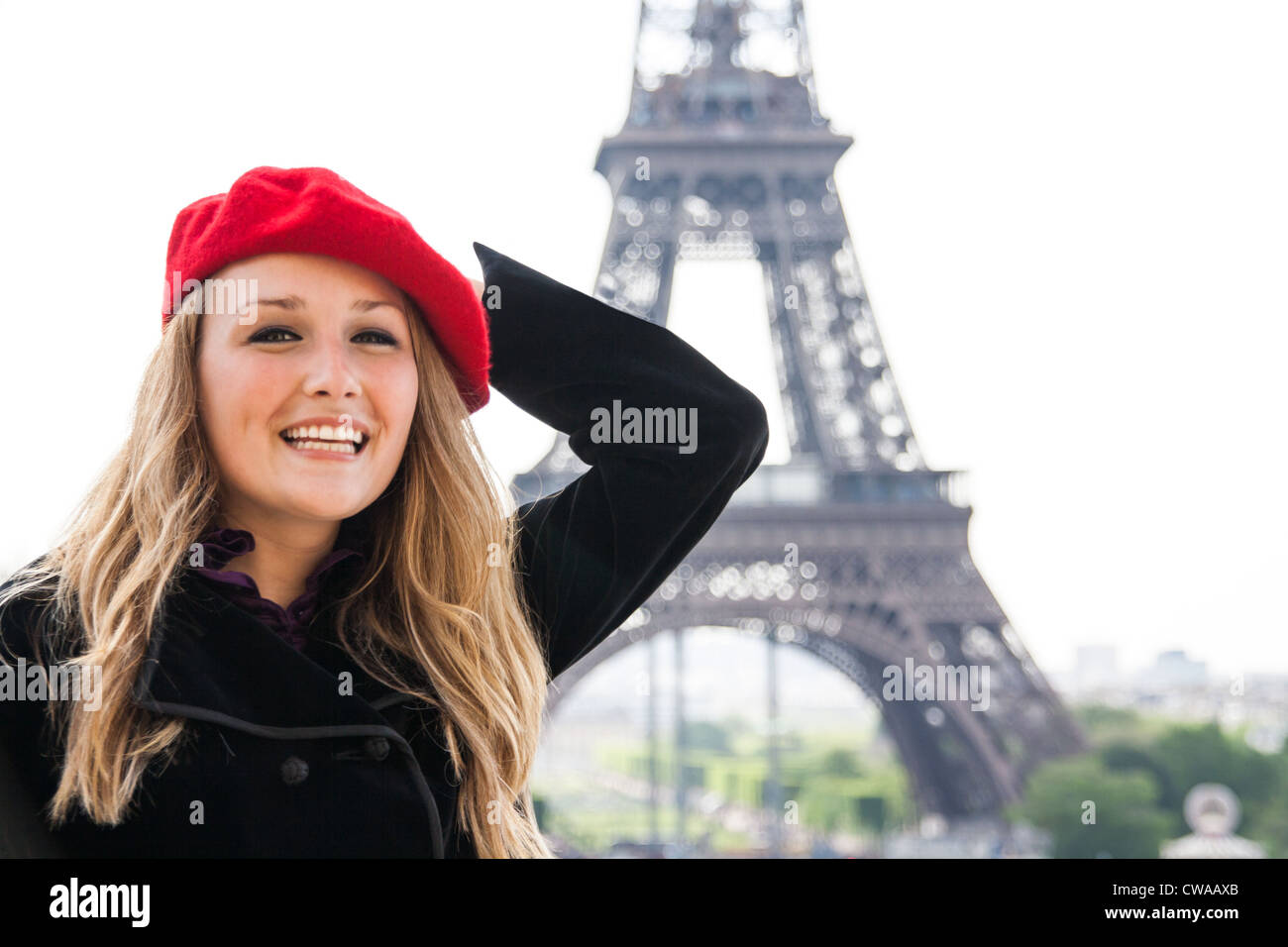 A Beautiful girl, wearing a red hat and smiling, in front of the Eiffel Tower. Stock Photo