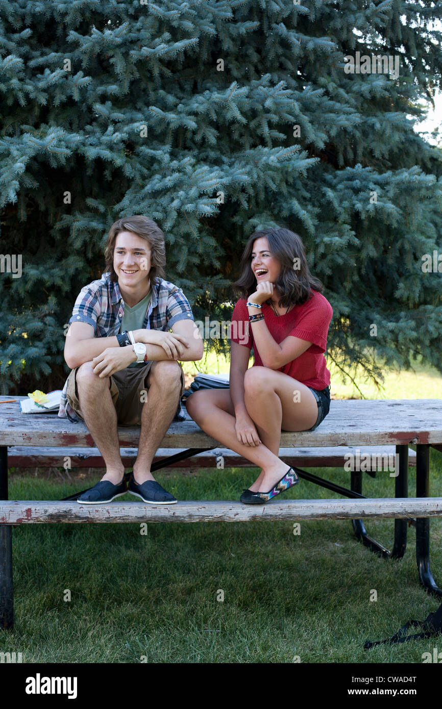 Teenage couple sitting on picnic table in park Stock Photo