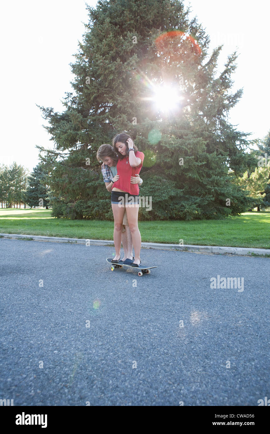 Teenage boy helping girlfriend ride skateboard Stock Photo