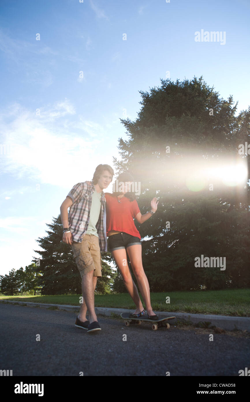 Teenage boy helping girlfriend ride skateboard Stock Photo