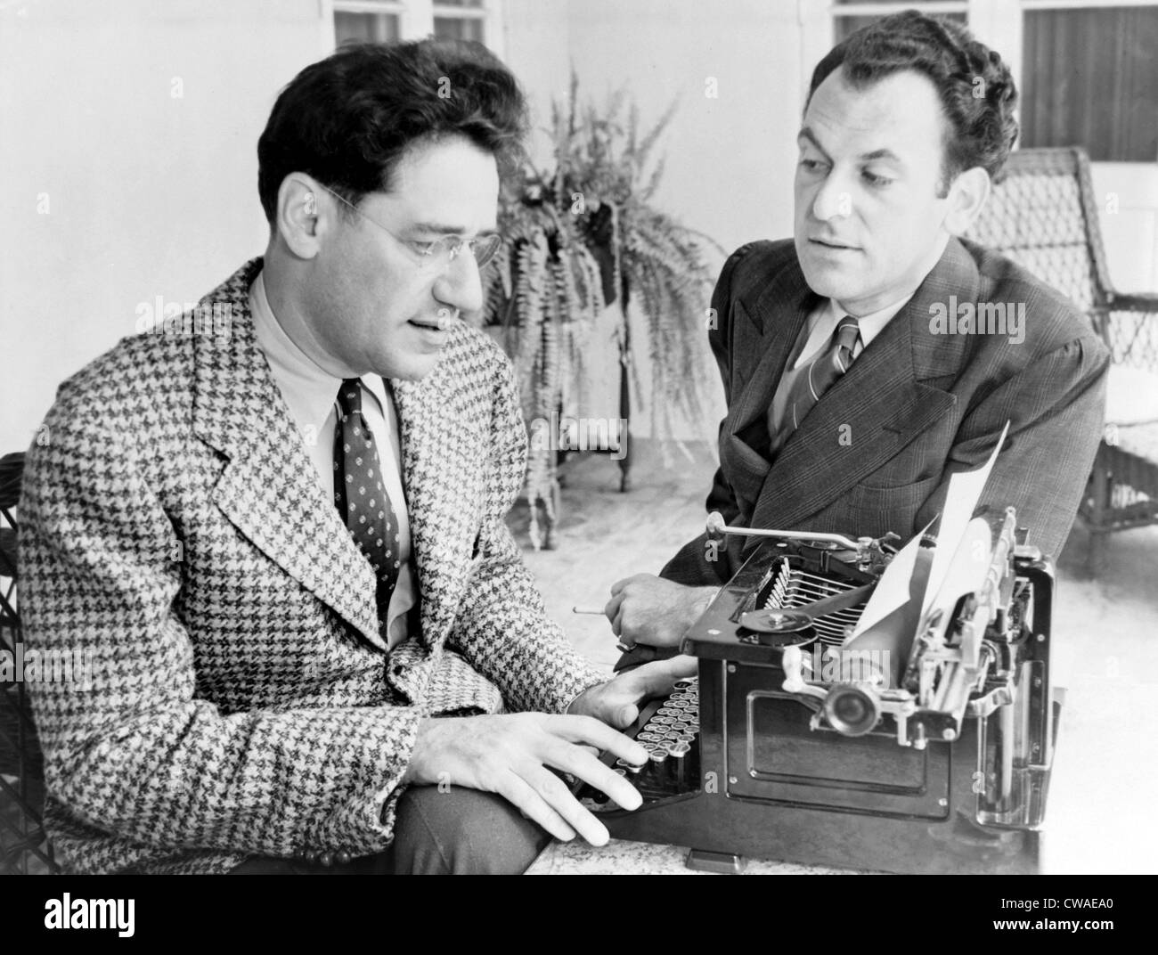 George S. Kaufman (1889-1961) typing while Moss Hart (1904-1961) talks, in 1937, the year their play, YOU CAN'T TAKE IT WITH Stock Photo