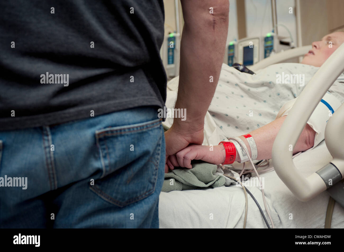 Man holding woman's hand in hospital room Stock Photo