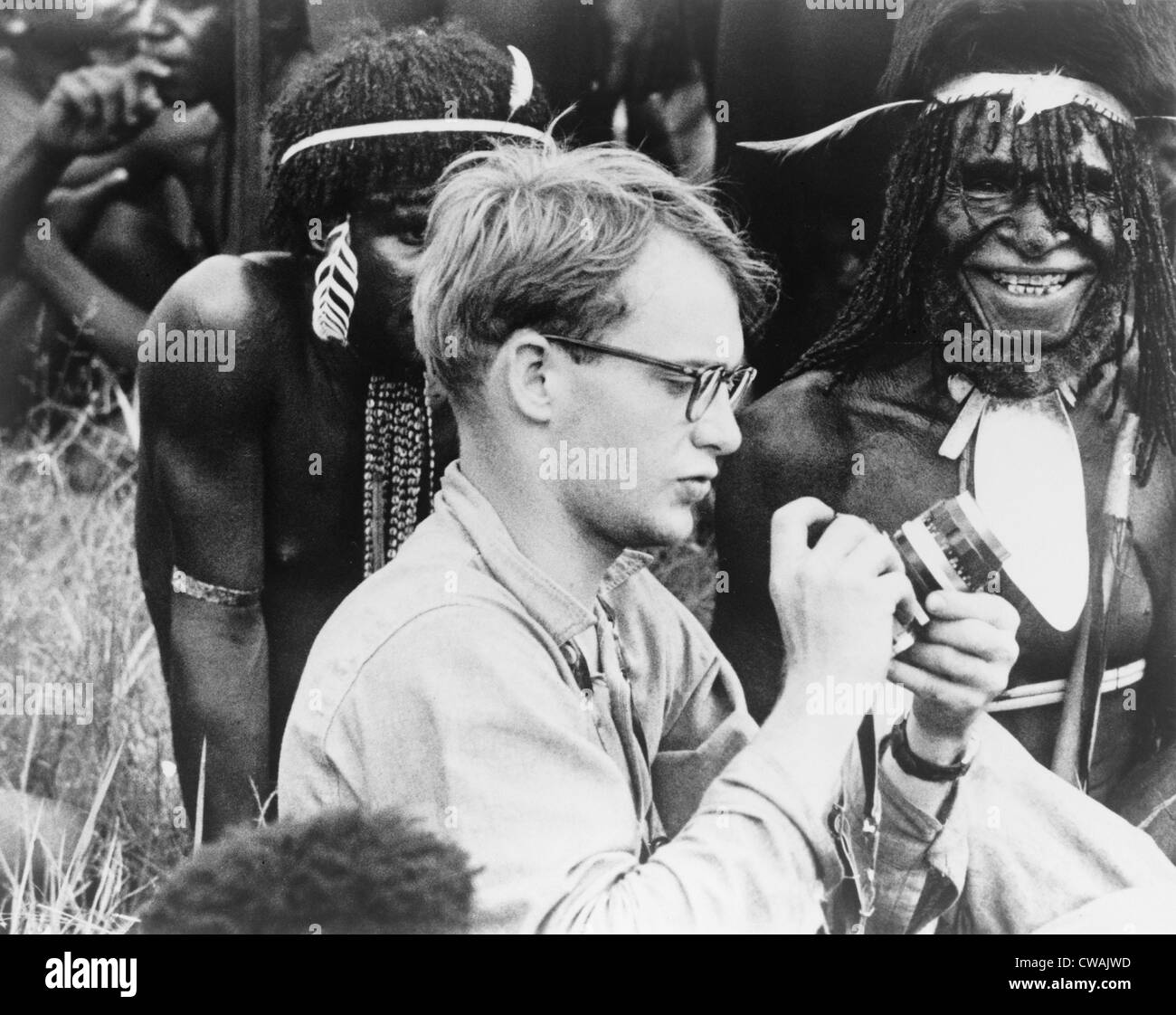 Michael C. Rockefeller (1934-1961) adjusting his camera in New Guinea, Papuan men in background.  He disappeared while swimming Stock Photo