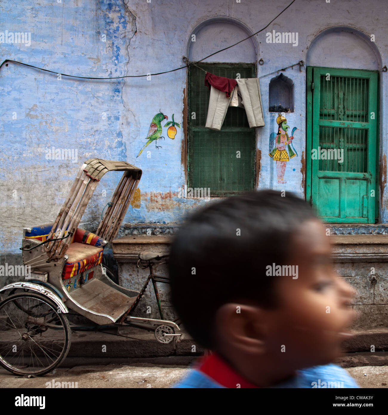 Child running through an alley where a rickshaw is parked against a ...