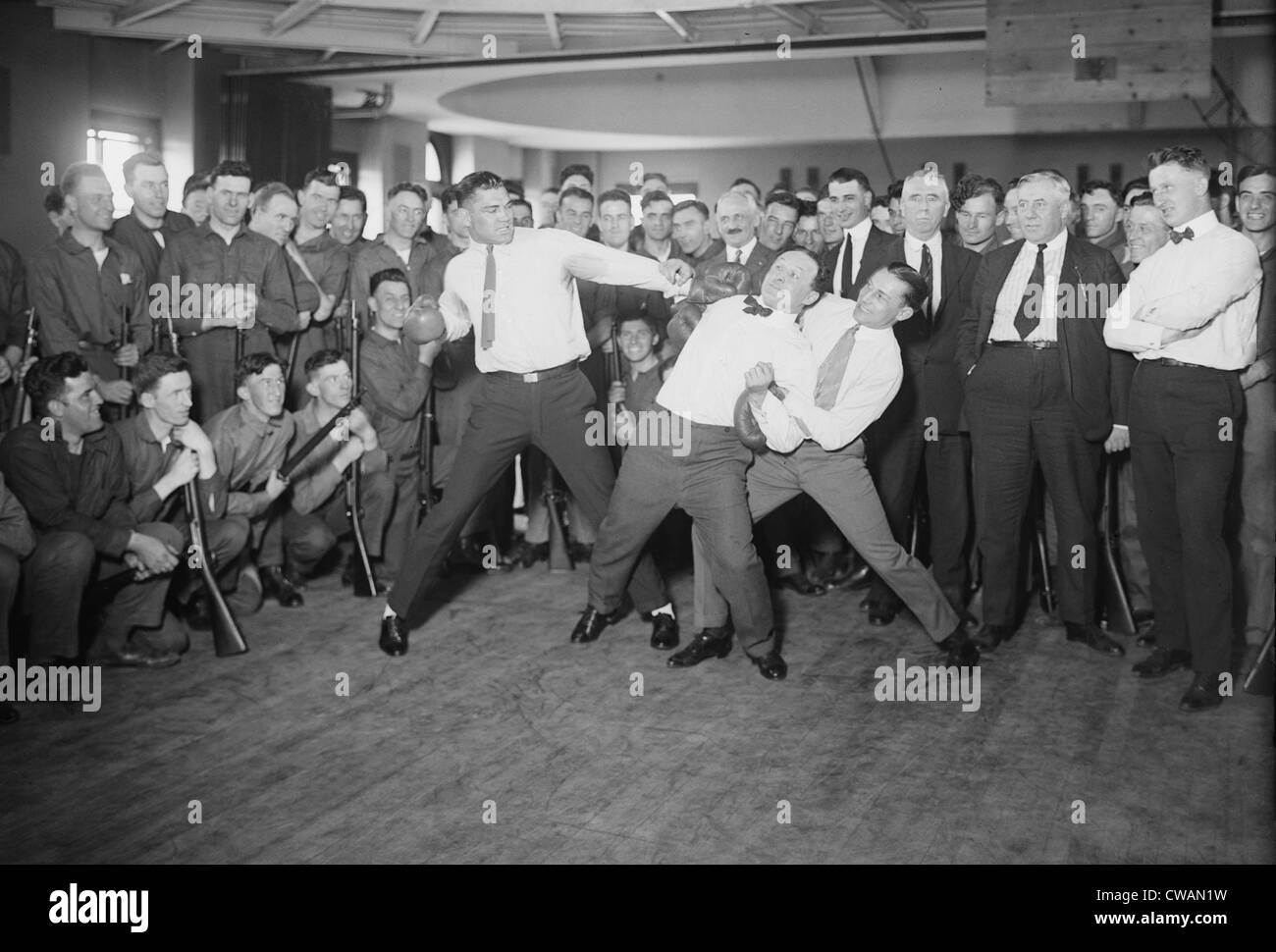 Harry Houdini cannot escape the hold of boxer Benny Leonard and Jack Dempsey prepare to swing.  Houdini claimed he could Stock Photo