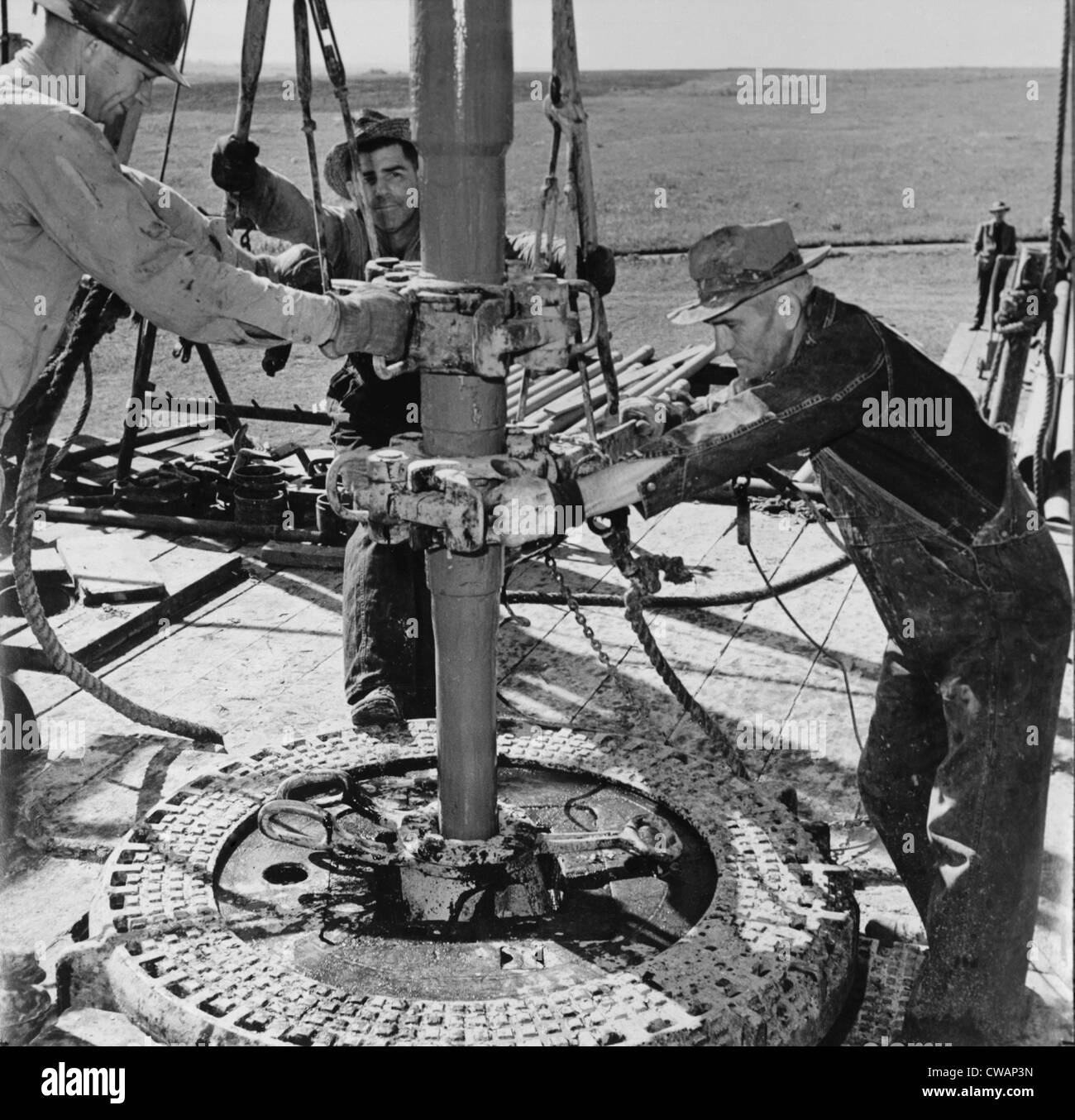Oil well worked by 'wildcat' drillers. Roughnecks, as derrick workers were called, use tools called 'tongs' which are clamped Stock Photo