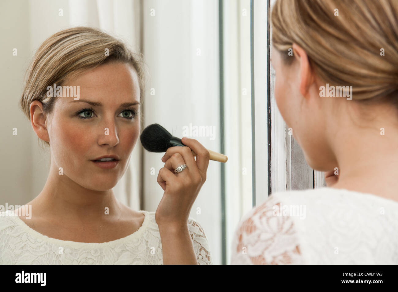 Woman in a white dress, applying blusher in a mirror Stock Photo