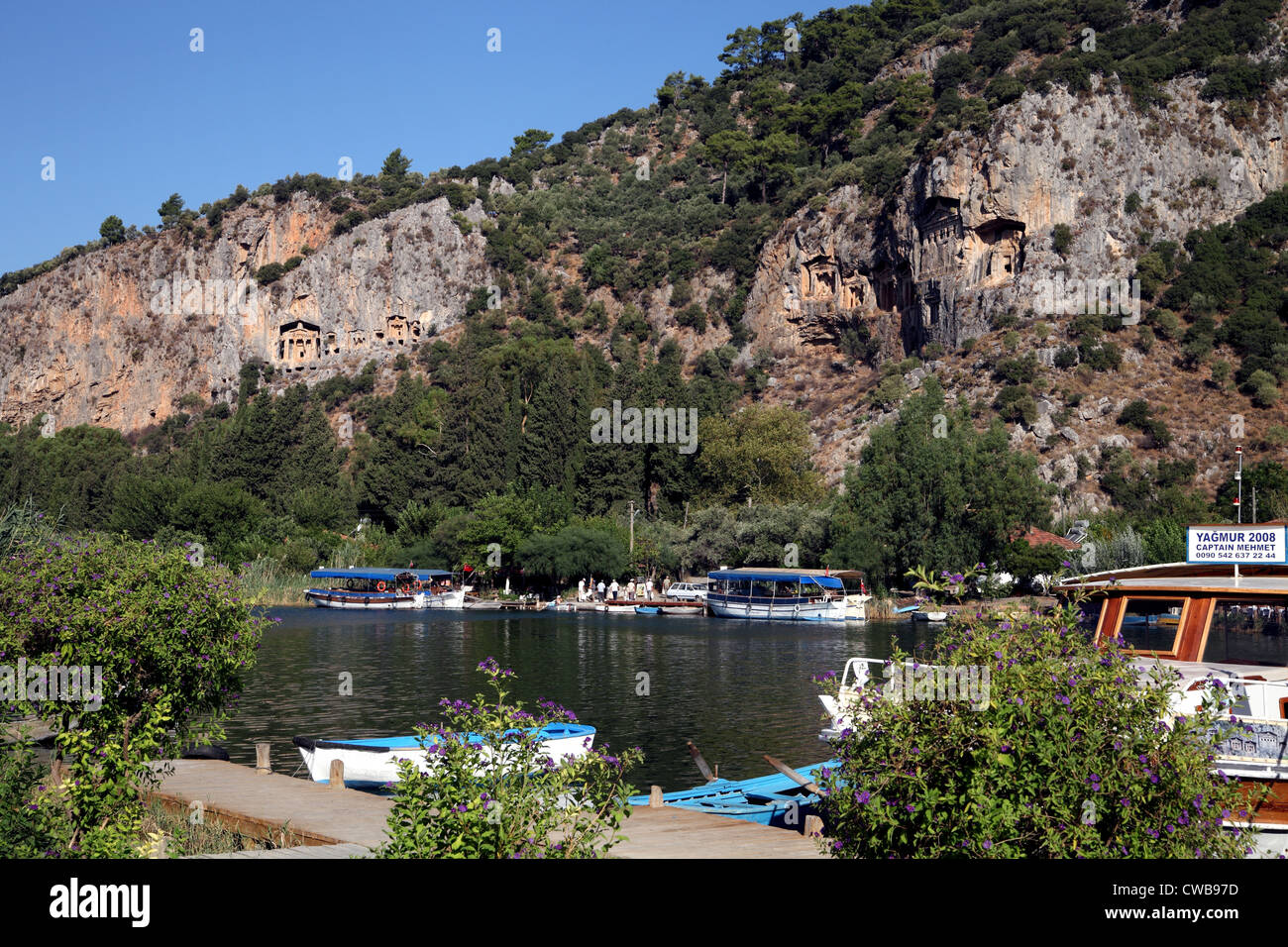 Landscape view of Lycian rock tombs across the river from Dalyan town, Turkey with river boats in the foreground Stock Photo