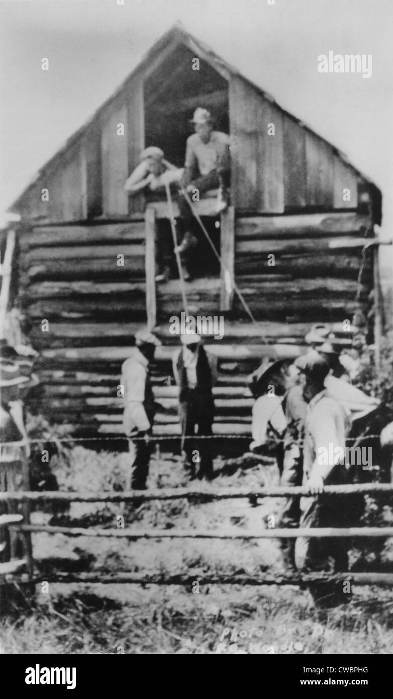 Photographic postcard of a few men preparing to lynch African American man by hanging from a barn.  Unlike most lynching photos Stock Photo