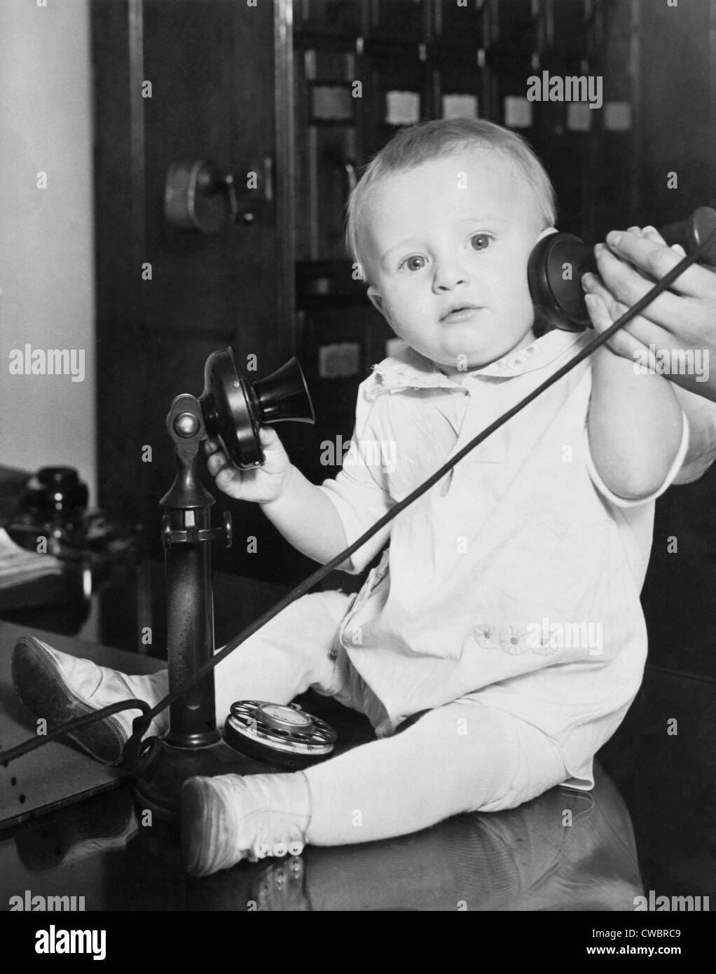 A baby found under a bed at the Stevens Hotel, Chicago, Illinois was photographed with a telephone to illustrate the many phone Stock Photo