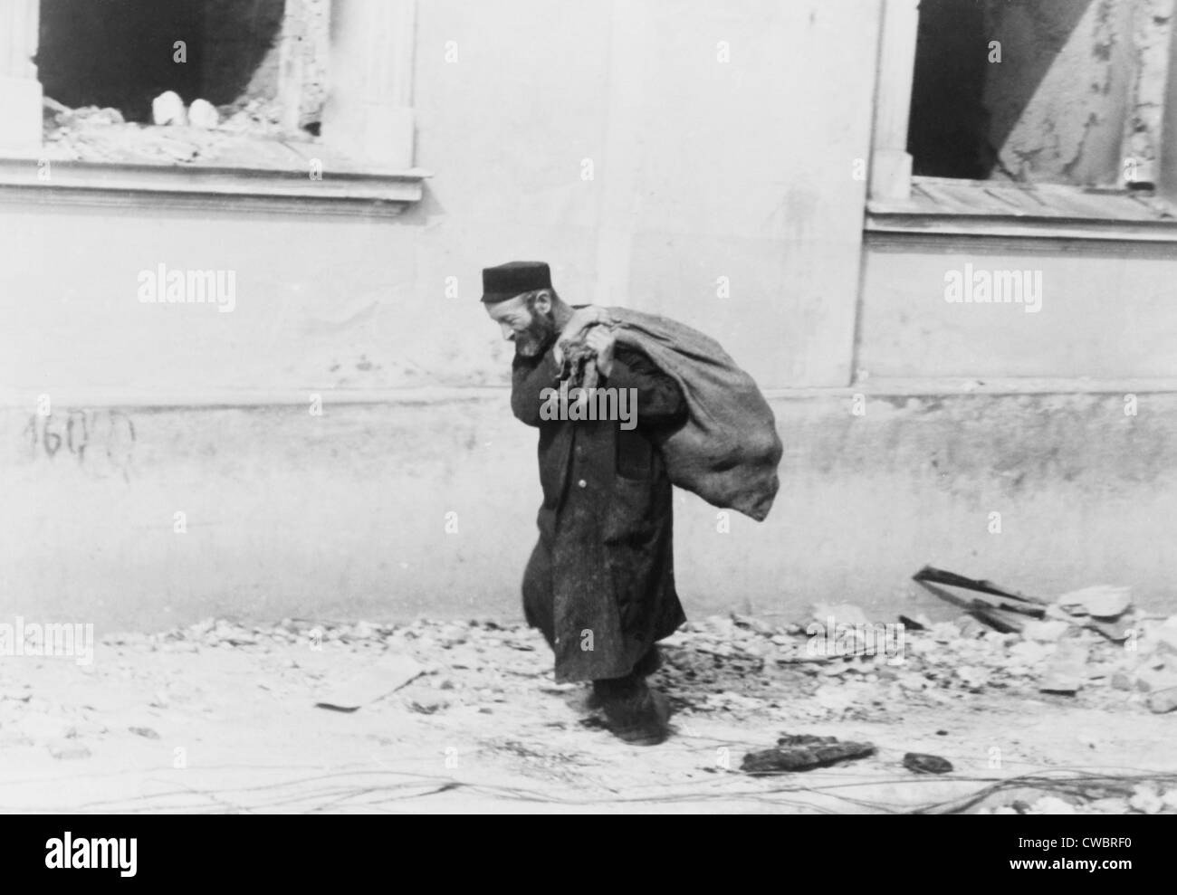 A solitary Jewish man carrying a sack walking past bomb damaged buildings in Poland in the early days of World War II. 1939-40. Stock Photo